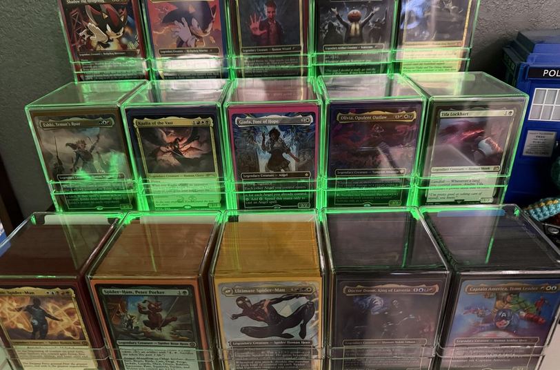 Fifteen Magic The Gathering commander decks in clear boxes lit by green LEDs
